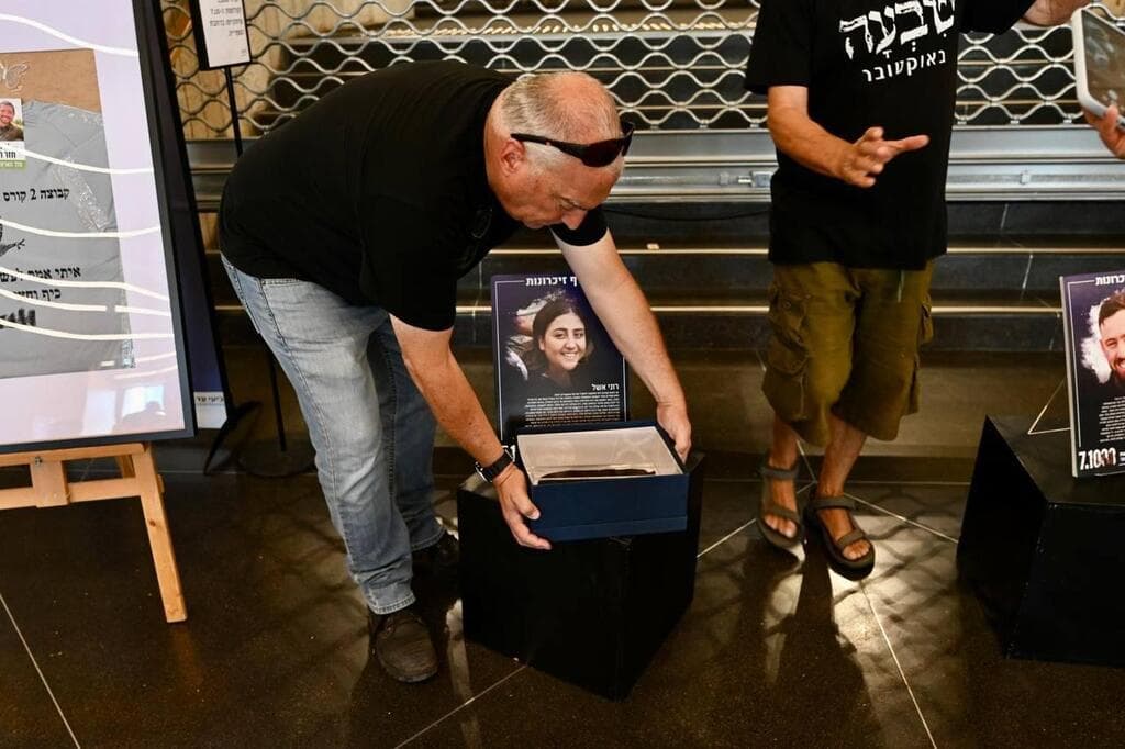 איל אשל מניח את כומתת בתו רוני ז"ל בתערוכה (צילום: מועצת אוקטובר) אייל אשל מניח את הכומתה של ביתו, רוני אשל ז"ל בתערוכת "1,000 זיכרונות"