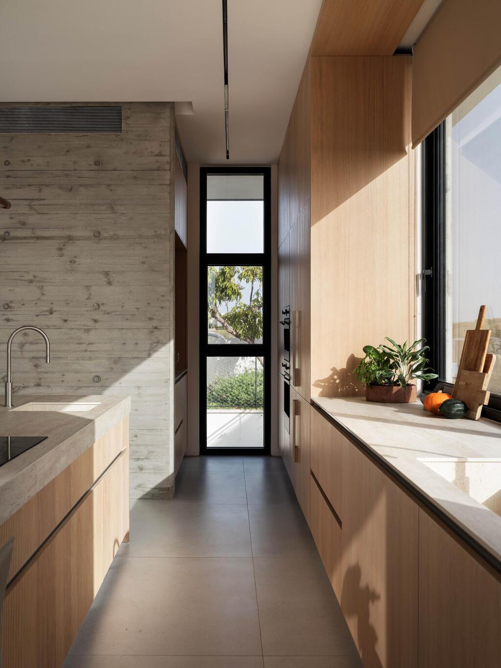 מטבח המורכב משני פסים מקבילים עם חזיתות בגוון אלון בהיר ומשטח מאבן טרוורטין (צילום: אלון ברהום) בית פרטי בקיסריה. תכנון ועיצוב: ישראל נוטס