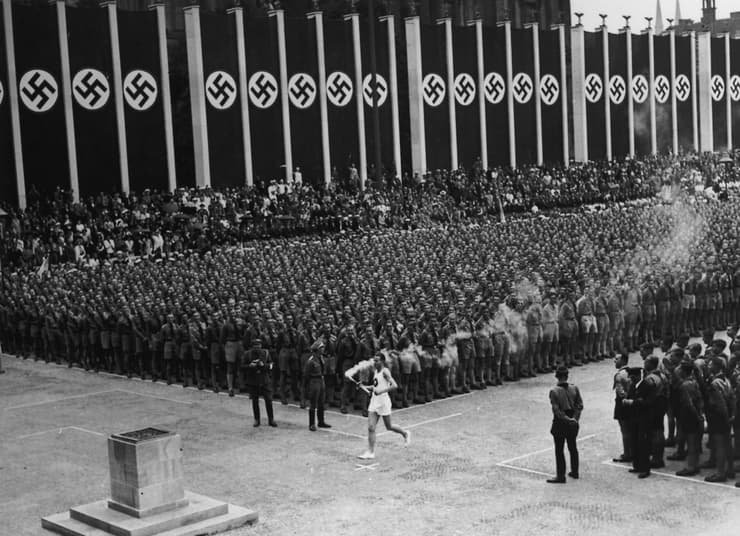 מדליקים את הלפיד האולימפי ב-1936, לצד דגלי גרמניה הנאצית