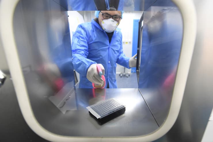 עובד בחליפת מגן בודק דגימות בתוך מעבדה בעקבות התפרצות נגיף הקורונה