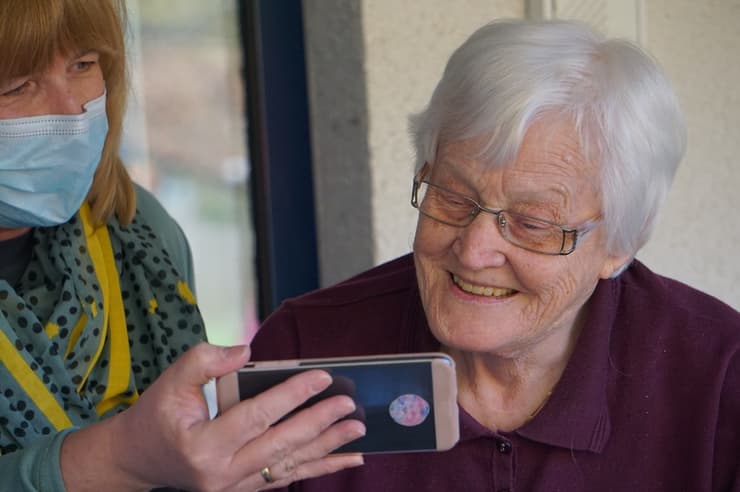 אישה מציגה טלפון נייד לקשישה 
