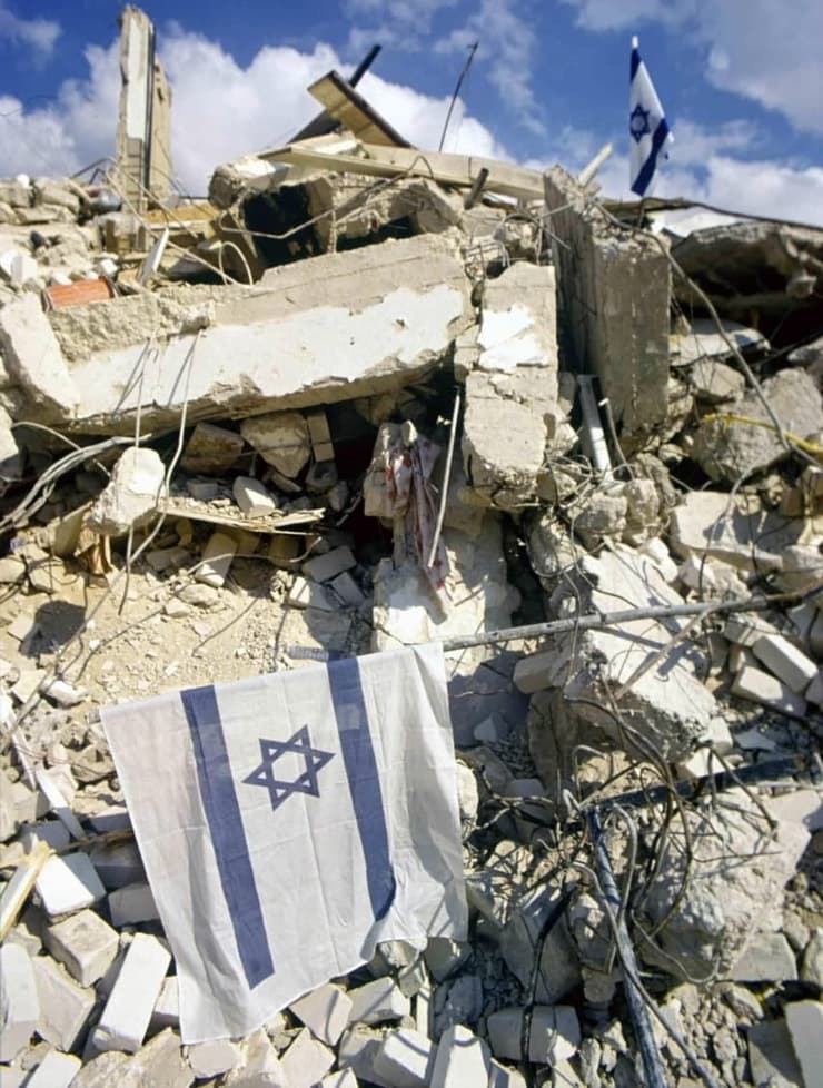 דגל ישראל מתנוסס על רקע חורבות מהטילים
