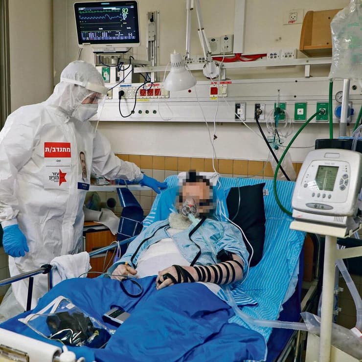 מתפללים להחלמה. מתנדב עזר מציון מסייע לחולה להניח תפילין, במרכז הרפואי שיבא