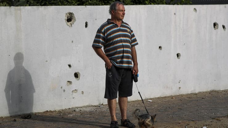 אדם מסתובב עם כלבו ליד גדר הבית שנפגעה מרקטה