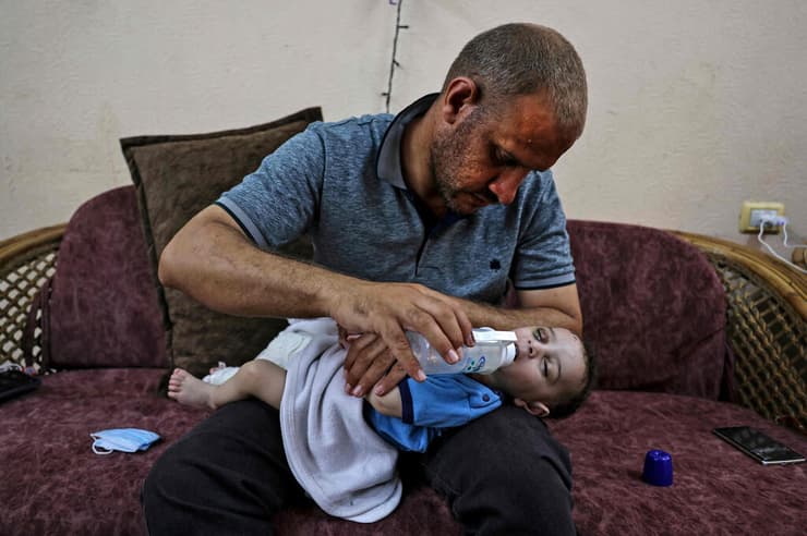 פלסטיני בעזה מאכיל תינוק בן חמישה חודשים שאמו וארבעת אחיו נהרגו בתקיפה ישראלית. רגלו של התינוק נשברה