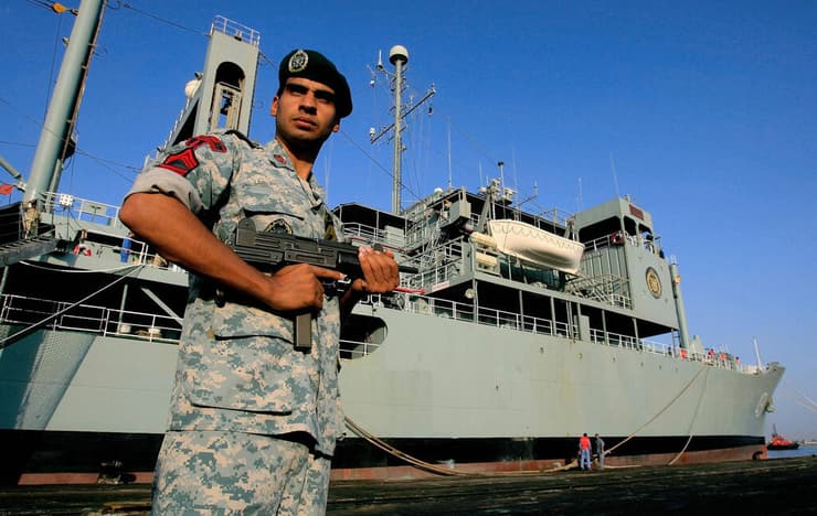 לוחם איראני עומד ליד הספינה שעלתה כעת באש, בתמונה מ-2012. הרובה שבו הוא אוחז: "עוזי" ישראלי