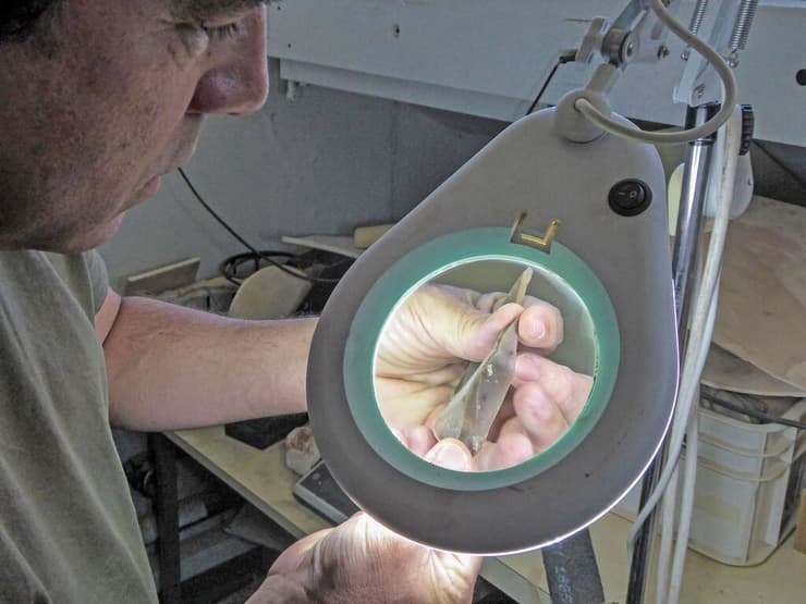 החוקר ד"ר עמרי ברזילי, פרהסטוריון ברשות העתיקות, בוחן תחת זכוכית מגדלת חוד מאבן צור מאתר בוקר תחתית