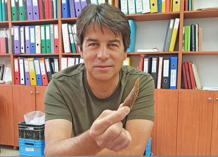 החוקר ד"ר עמרי ברזילי, פרהסטוריון ברשות העתיקות, בוחן תחת זכוכית מגדלת חוד מאבן צור מאתר בוקר תחתית