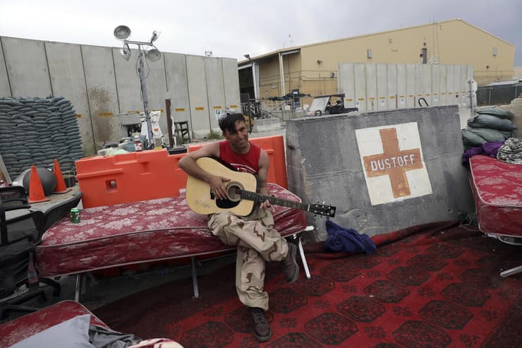 הבוזזים השאירו בקבוקים ופחיות. חייל אפגני מוצא זמן לנגן בגיטרה בבסיס בגראם  
