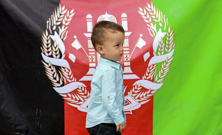 ילד פליט אפגני מול דגל אפגניסטן בהפגנה ב-19 באוגוסט עקב השתלטות הטליבאן טליבאן על המדינה מול שגרירות ארה"ב באוזבקיסטן