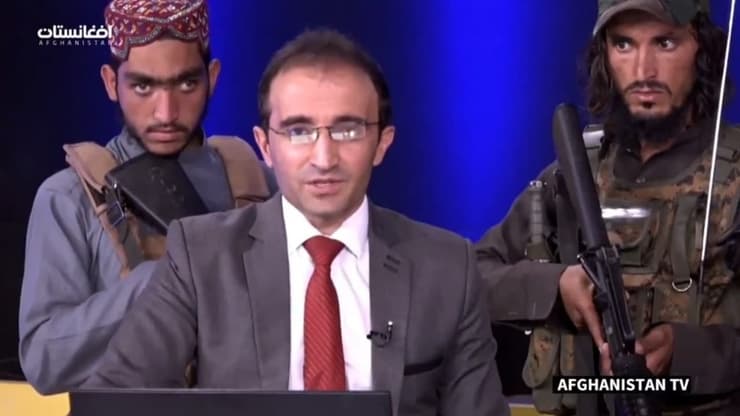 לוחמי טליבאן חמושים מאחורי מגיש טלוויזיה ב אפגניסטן