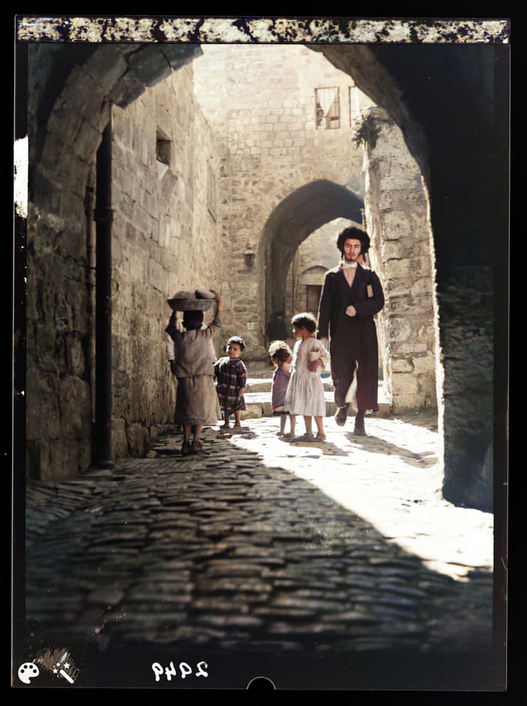 צעיר חרדי חולף ליד קבוצת ילדים בסמטאות העיר העתיקה בירושלים, אמצע שנות ה-20