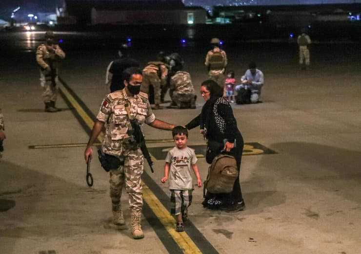 חייל של חיל האוויר של קטאר מלווה ילד מ אפגניסטן שפונה מ קאבול ב בסיס אל-עודייד ב קטאר 2 בספטמבר