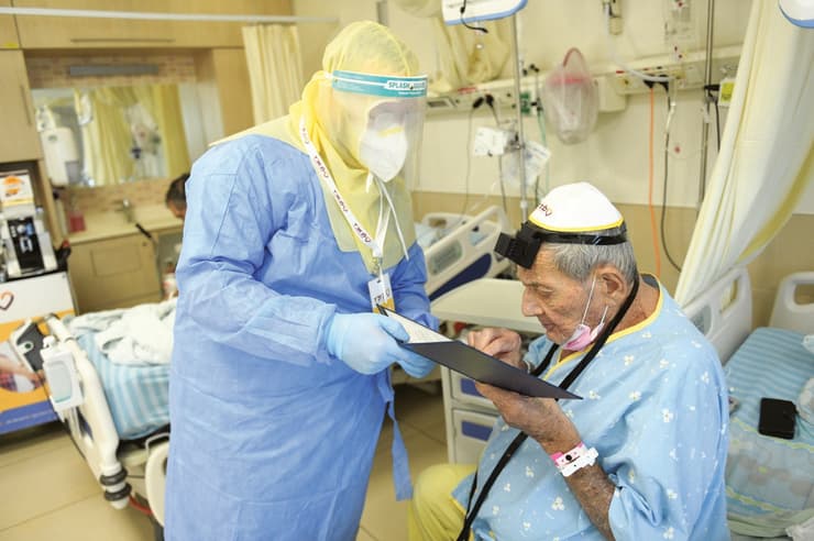 הרב מנדי ליפקין מ"לב חב"ד - אגף הפעלות בבתי רפואה של צעירי חב"ד", מסייע ליהודי להניח תפילין בתוך מחלקת הקורונה כשהוא ממוגן מכף רגל ועד ראש (צילום: מאיר אלפסי) הרב מנדי ליפקין מ"לב חב"ד - אגף הפעלות בבתי רפואה של צעירי חב"ד", מסייע ליהודי להניח תפילין בתוך מחלקת הקורונה כשהוא ממוגן מכף רגל ועד ראש