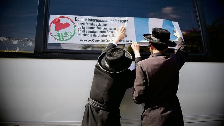 חברי 'לב טהור' תולים שלט לגיוס כספים למען המשפחות בכת, על גבי אוטובוס בגואטמלה