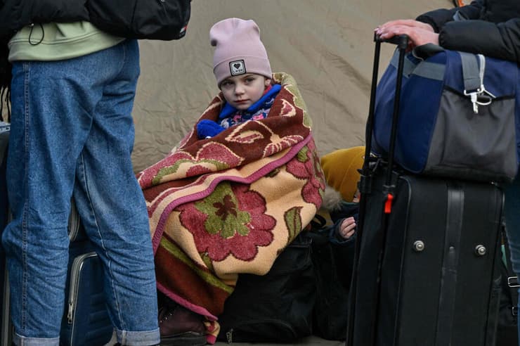 ילד אוקראיני יושב על מזוודות בגבול פולין