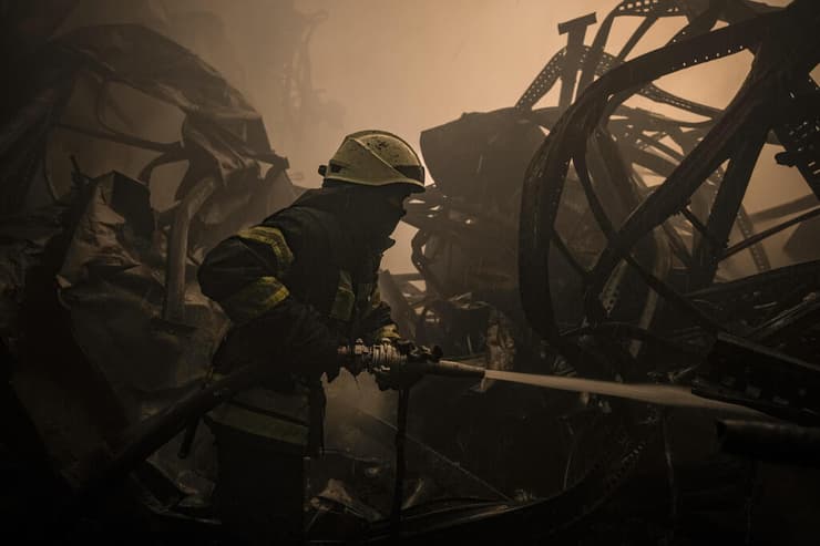 לוחם אש כבאי אוקראיני מכבה שריפה במרכז איחסון מזון ש נפגע ב מתקפה אוורית מחוץ ל קייב משבר מלחמה רוסיה אוקראינה 