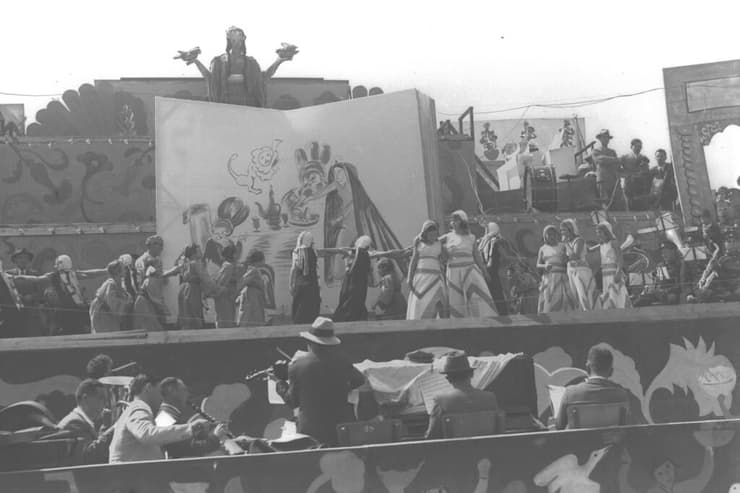 בימת בידור בעדלאידע של תל אביב ב-1935, הכוללת תזמורת ונערות רוקדות, לצד איור של אסתר המלכה במשתה עם אחשוורוש והמן