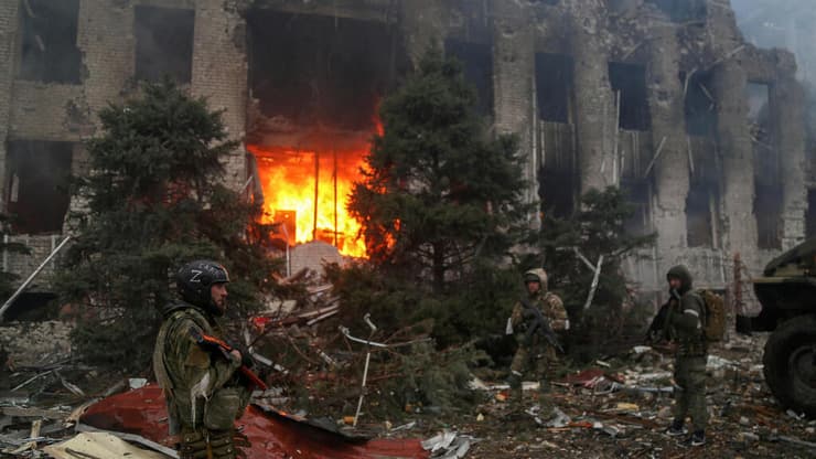 אנשי כוחות פרו רוסים וכוחות מיוחדים צ'צ'נים עומדים ליד בניין בוער בעיר מריופול משבר מלחמה רוסיה אוקראינה 