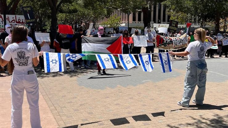 שליחות הסוכנות היהודית מניפות דגלי ישראל אל מול מפגינים פרו-פלסטינאים בקמפוס. אורנג' קאונטי, קליפורניה. (צילום: מיה וורביוב) שליחות הסוכנות היהודית מניפות דגלי ישראל אל מול מפגינים פרו-פלסטינאים בקמפוס. אורנג' קאונטי, קליפורניה.