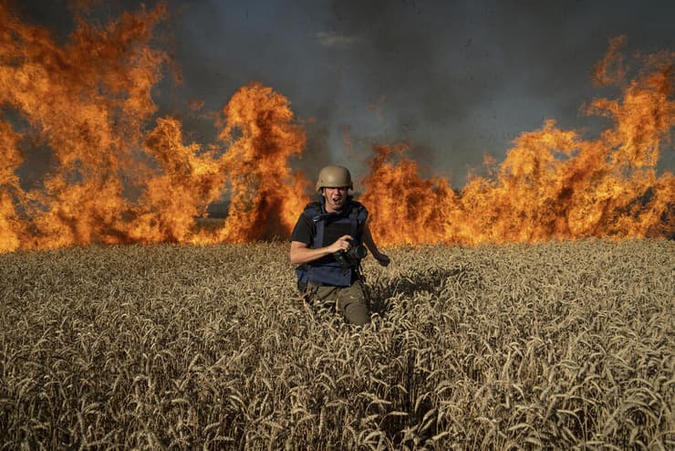 צלם בורח מ שריפה ב שדה חיטה שהופצץ על ידי רוסיה במחוז חרקוב באוקראינה