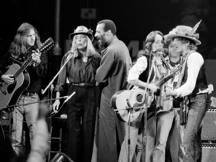 ג'וני מיטשל על הבמה עם אמני פולק נוספים, ובהם בוב דילן וג'ואן באאז, 1975