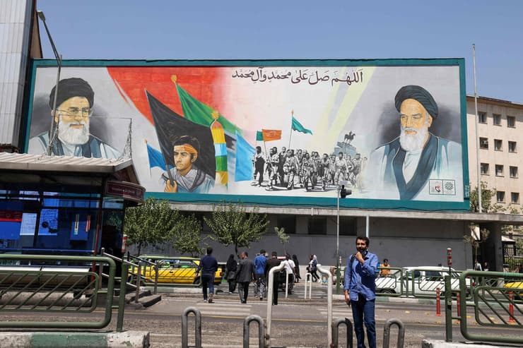 איראן איראנים הולכים בבירה טהרן ליד שלט של האייתוללות עלי חמינאי ו רוחאללה חומייני יום אחרי הניסיון לרצוח את סלמן רושדי