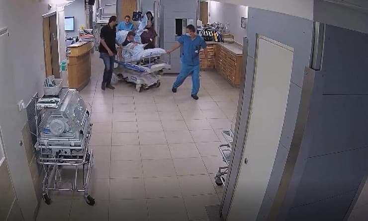 הרופא ד"ר גאנם (מכוסה בשמיכה), על מיטת היולדת שכבר נכנסה ללידה פעילה, והועברה על המיטה לחדר הניתוח. הוא מחזיק בשלב זה את ראשה שלח התינוקת שלא ייגע בחבל הטבור