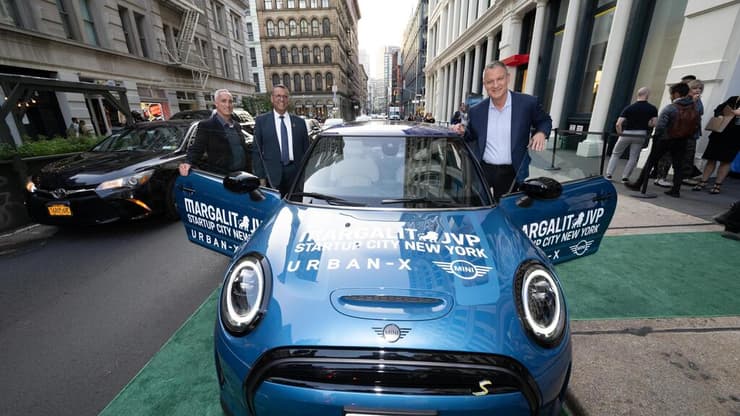 בלב ליבו של רובע הסוהו במנהטן נעצרת מכונית MINI  חשמלית כחולה על שטיח ירוק בפתח מרכז החדשנות. 