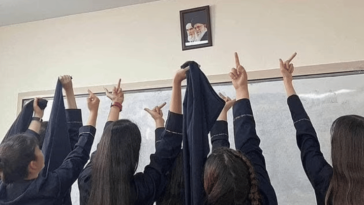 תלמידות תיכון ב איראן מפנות אצבע משולשת לתמונותיהם של המנהיג העליון עלי חמניאי וקודמו רוחאללה חומייני בכיתה בבית ספר תמונה שהופצה ברשתות החברתיות ופורסמה גם בגרדיאן הבריטי