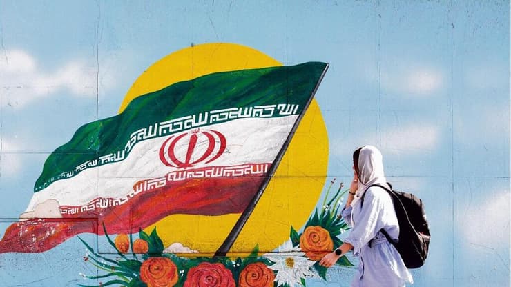 צעירה בטהרן על רקע ציור קיר של דגל איראן