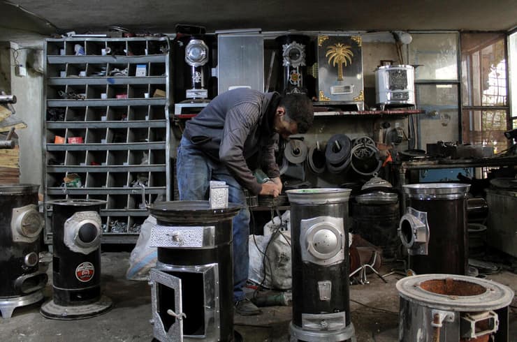 סוריה קור חורף גבר עובד ב חנות ש מייצרת תנורי חימום להסקה עם ענפי פיסטוק בעיר חמה