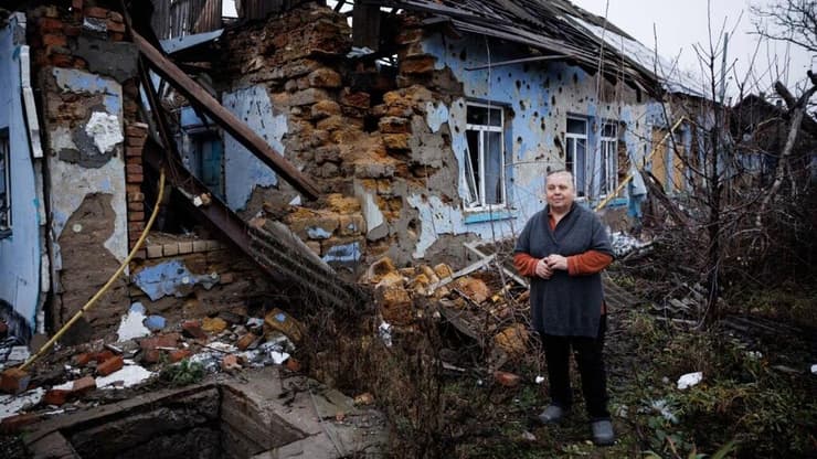 אישה עומדת ליד ביתה שהופצץ על ידי הרוסים