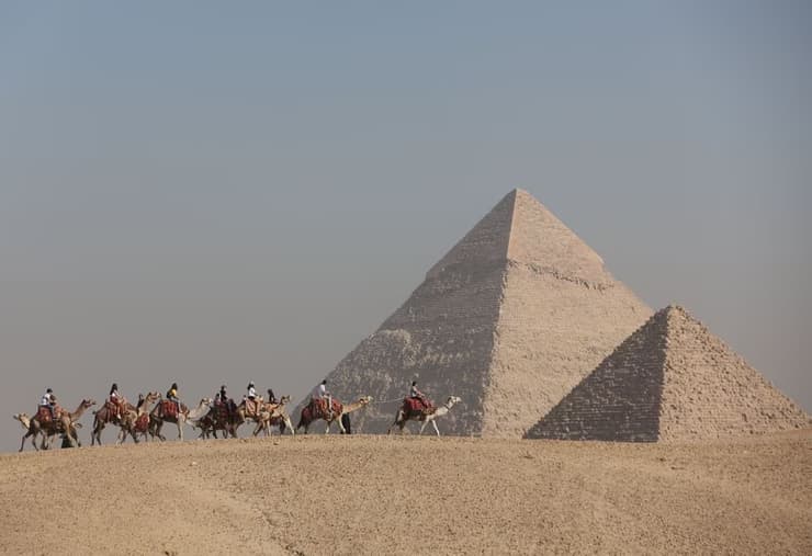 Tourists ride camels in front of the Great Pyramids plateau in Giza, Egypt December 11, 2022 