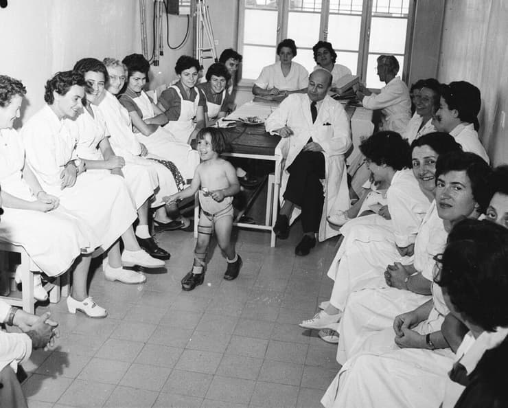 ילדה שנפגעה מנגיף הפוליו בשנות ה־50, מוקפת בצוות מטפלים