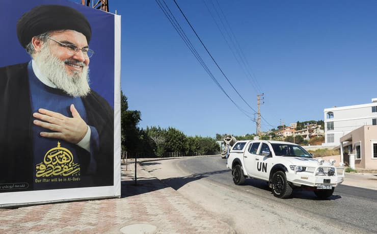רכב של פקחי או"ם חולף ליד שלט עם תמונה של חסן נסראללה בדרום לבנון