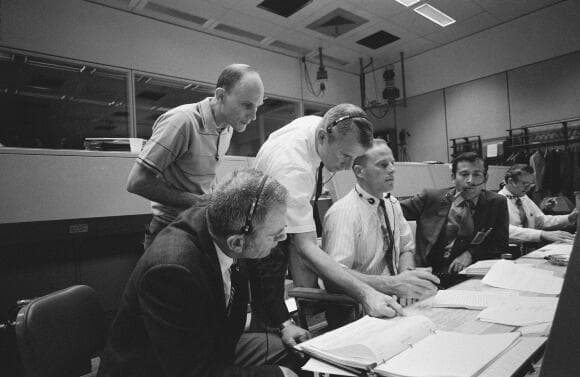 בלי תפקיד רשמי, הוא תרם תרומה חשובה להצלת חבריו למשימה. מטינגלי (מאחור) עם צוות חדר הבקרה במהלך משימת אפולו 13, אפריל 1970