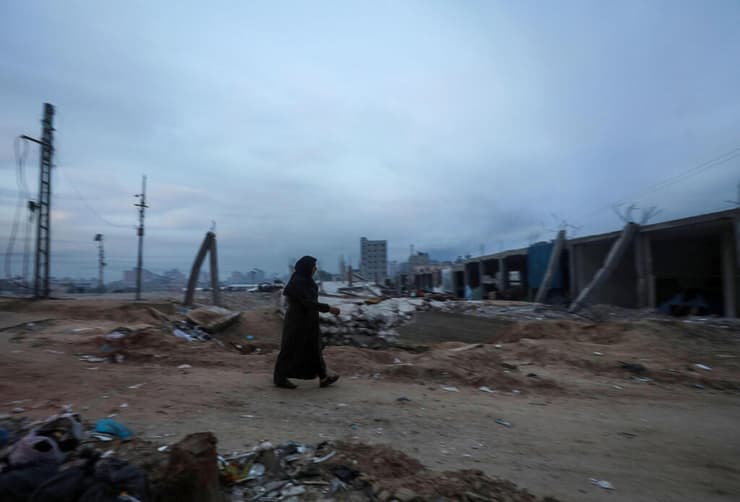אישה הולכת ליד הריסות הבניינים שנהרסו במחנה הפליטים אל נוסייראת, רצועת עזה
