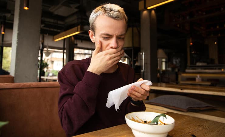 גבר צעיר סובל מאלרגיה למזון בעת ביקור במסעדה