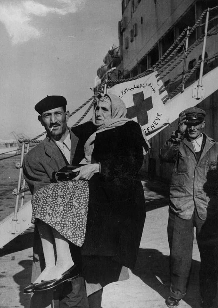 פליט יהודי ממצרים נושא את אימו הקשישה בירידה מהסיפון בנמל פיראוס, 1957