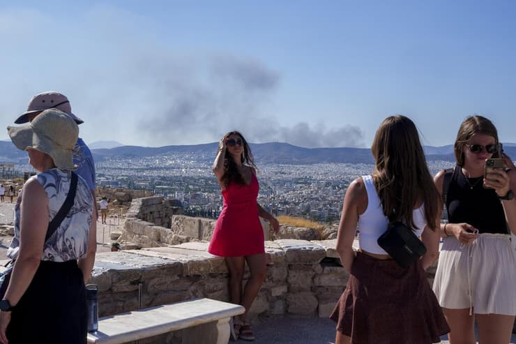 תיירת מצטלמת באקרופוליס כשמאחוריה ברקע עשן של שריפות