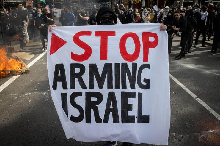 מפגינים עם הכרזה "הפסיקו לחמש את ישראל", כולל המשולש האדום המזוהה עם סרטוני התעמולה של חמאס (צילום: Darrian Traynor/Getty Images) אוסטרליה מלבורן מהומות מפגינים נגד ישראל