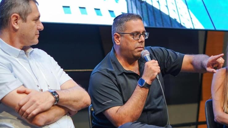 "אין לנו ידיים עובדות". עמוס דבוש וארנון פרידמן בכנס (שיר חן) עמוס דבוש בכנס נדל"ן