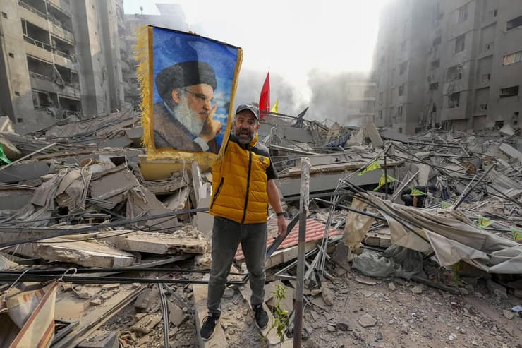 אדם מציג תמונה של נסראללה בהריסות בדאחייה בביירות (צילום: AP / Hassan Ammar) גבר מוחה נגד ישראל בדאחייה שבביירות, דרום לבנון