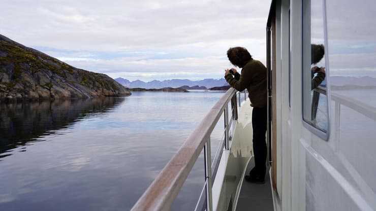 אישה מצלמת מספינת תיירים בין מאניצוק לסיסימיות, בחוף המערבי של גרינלנד.