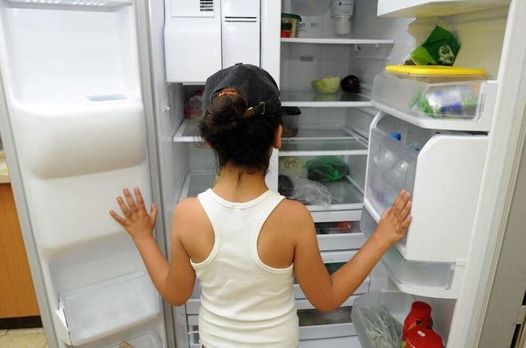 ילדה ניצבת מול מקרר כמעט ריק