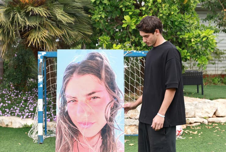 טל נעים ליד תמונה של אחותו (צילום: דנה קופל) טל נעים, אחיה של מאי שנרצחה במיגונית ליד קיבוץ רעים