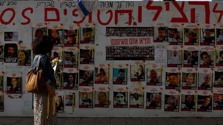 מחכים לשובם. עוברת אורח מביטה על תמונות החטופים בעזה על קיר בתל אביב (צילום: REUTERS/Hannah McKay) אישה מביטה על תמונות החטופים בעזה על קיר בתל אביב