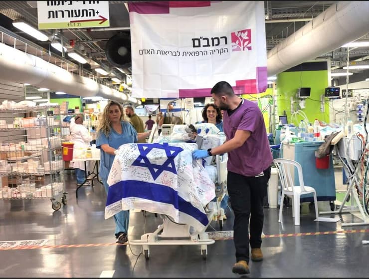 מיטתו של לוחם שנפצע בלבנון מועברת מטיפול נמרץ להמשך שיקום, עם דגל ישראל
