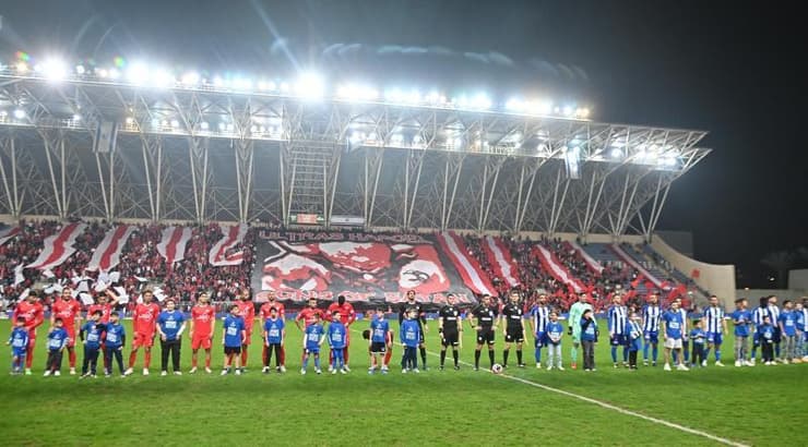 שחקני הפועל פתח תקווה והפועל תל אביב על רקע קהל אוהדי הפועל תל אביב